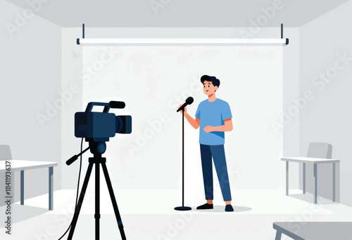 A man in blue speaks into a microphone in a studio, facing a video camera on a tripod