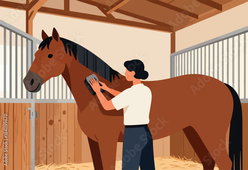 A person grooming a brown horse in a barn stall. Straw is on the ground