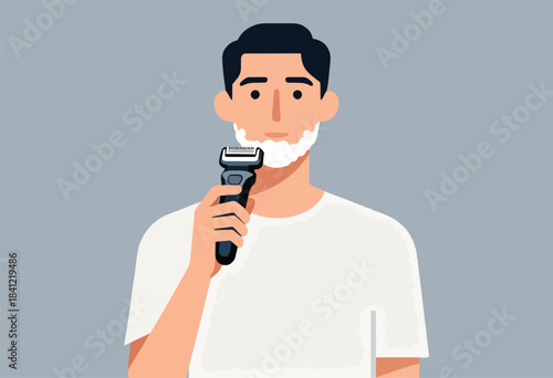 A man shaves his face with an electric razor, he is wearing a white tee and his face has a white foam