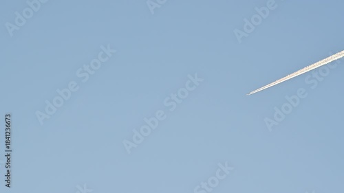 Airplane flying high up in the sky leaving a vapor trail in the clear blue sky.