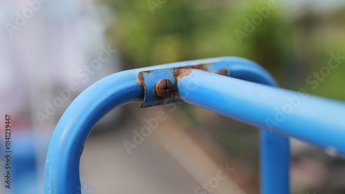 Close-up View of Rusty Blue Metal Bar on Playground Equipment Surrounded by Greenery