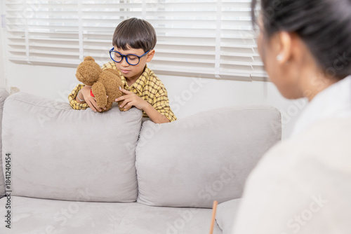 Schilderij op canvas Young child sitting on sofa hugging teddy bear tightly, avoiding eye contact wit