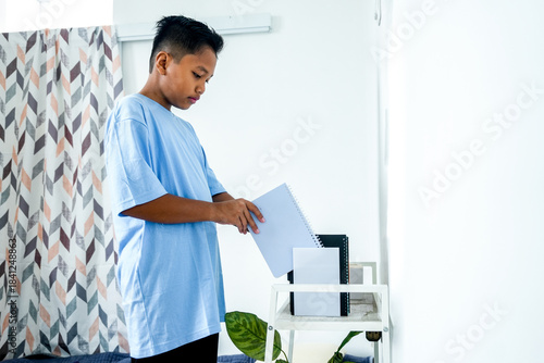 Young Boy Organizing His School Books And Notebooks On White Metal Shelf In His Room