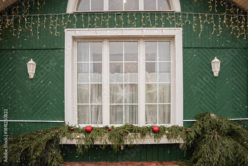 A large window in a green house decorated with festive Christmas garlands and lights.