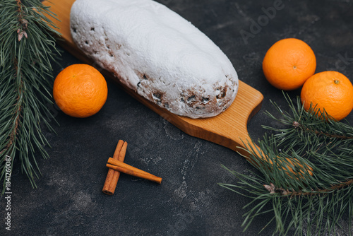 Christmas stolen in powdered sugar on a dark background with pine branches and tangerines. Traditional Christmas delicacies. Top view