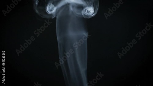 Wispy white smoke elegantly curls upwards, forming abstract shapes on a deep black background