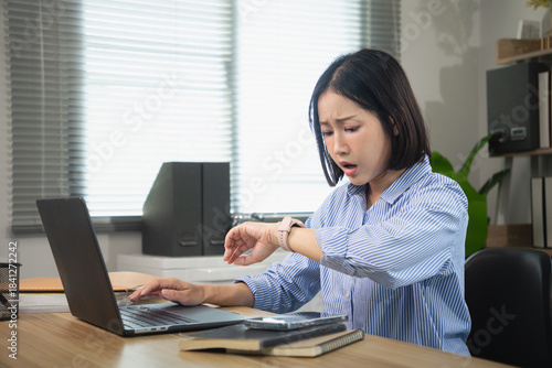 Slika na platnu Shocked Asian female employee looking at her watch due to a tight deadline or ur