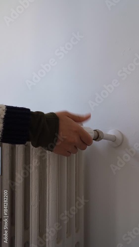 Person's hand turning the thermostatic valve on a white radiator to control room temperature