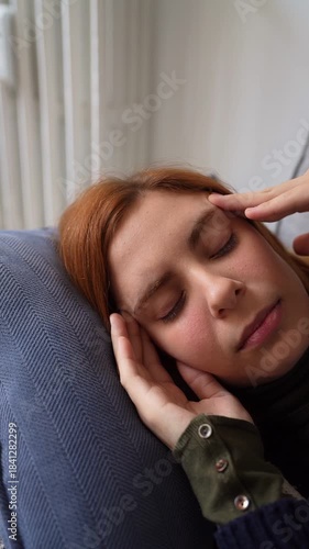 Close-up of a young woman with a terrible headache massaging her temples while lying on a sofa