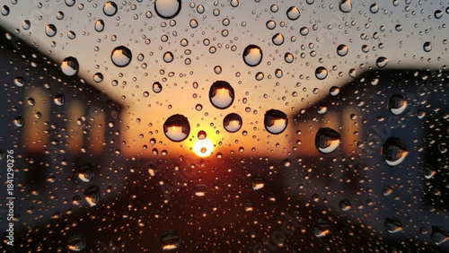 Mesmerizing close-up of raindrops clinging to a window pane, perfectly framing a blurred, warm sunset between residential buildings, creating a serene and reflective atmosphere