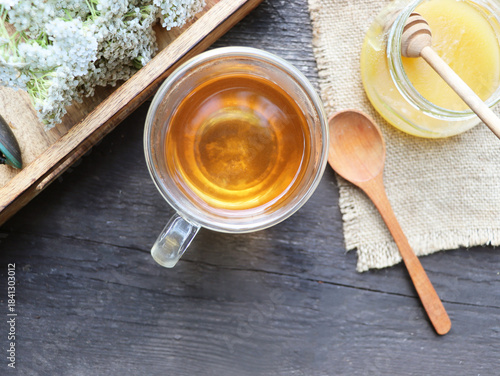 Yarrow tea in a glass cup with honey, fresh yarrow flowers on tray