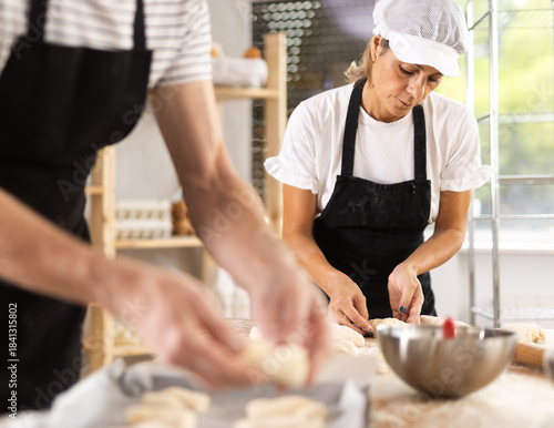 Two bakers place pieces of dough on a baking tray to make croissants