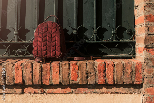 Red velvet backpack resting on brick fence with empty space for text or post. Mockup template image of red backpack on the street for product promotion.