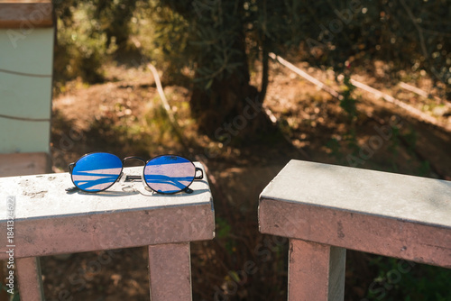 Blue sunglasses resting on metal fence at the park with empty space for text or social media post. Mockup template of sunglasses with hard light outdoors.