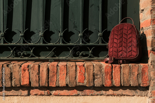 Red velvet backpack resting on brick fence with empty space for text or post. Mockup template image of red backpack on the street for product promotion.