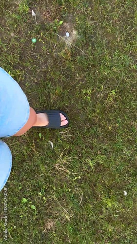 Close-up view of a foot in black sandals stepping on grass, showcasing the texture of the ground and footwear, with a gradual camera tilt revealing the surroundings