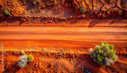 Aerial view capturing a vibrant orange dirt road traversing arid, cracked earth with sparse desert vegetation.