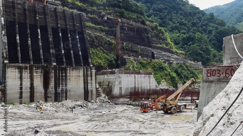 Heavy machinery working at hydropower dam construction site in Nepal featuring yellow excavators and dump trucks amidst steel rebar reinforcement and concrete structures for energy.