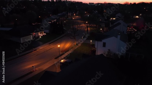 Wallpaper Mural Quiet American suburb at night illuminated by soft amber streetlights, showing houses, lawns and winding residential road. Window lights contrast with dark neighborhood atmosphere. Aerial approaching. Torontodigital.ca