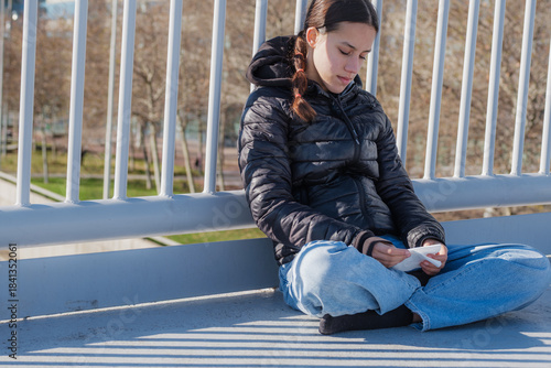 Teenager sitting outdoors contemplating letter on bridge