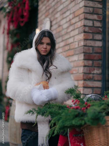 Serious Woman in White Fur Coat Holding Baked Roll near Christmas Decor