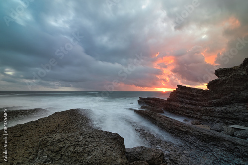Sunset at Cresmina beach in Cascais, Portugal. Geological formations of limestone and dramatic clouds in the sky.