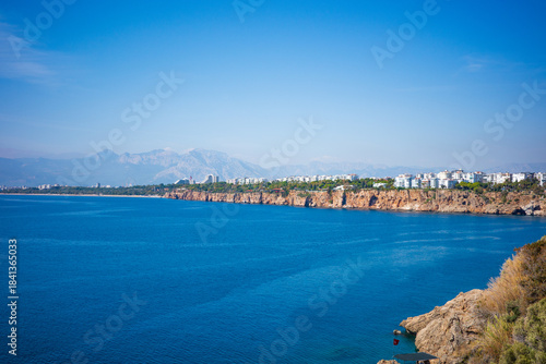 Wallpaper Mural A stunning panoramic view of the Mediterranean coastline featuring deep blue water, rugged rocky cliffs, and a distant cityscape framed by majestic mountains Torontodigital.ca