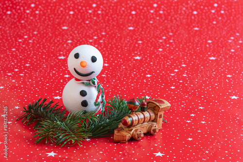 little handmade snowman with fir branches and toy locomotive on red background with copy space