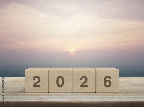 2026 letter on wood block cubes on wooden table over city tower and skyscraper at sunset, vintage style, Happy new year 2026 cover concept