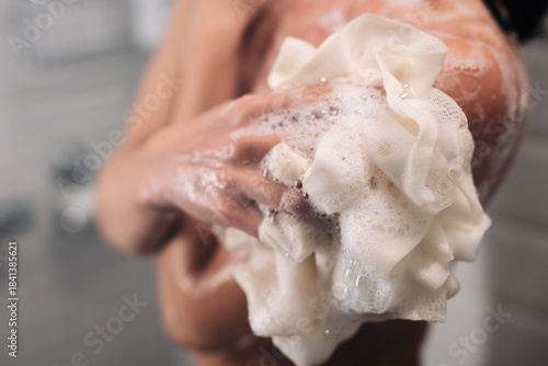 Obraz na plátně Close-up of a person in a shower using a loofah with soap bubbles, showcasing pe
