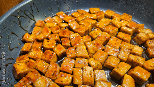 Grilled tofu cubes frying in a pan on the stove. Plant-based meat replacement in a sticky soy sauce. Meal-prep cooking and easy recipe inspiration.