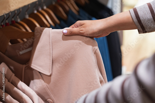 Close-up of a shopper's hand touching the collar of a pink beige jacket to check the fabric quality and texture in a retail store