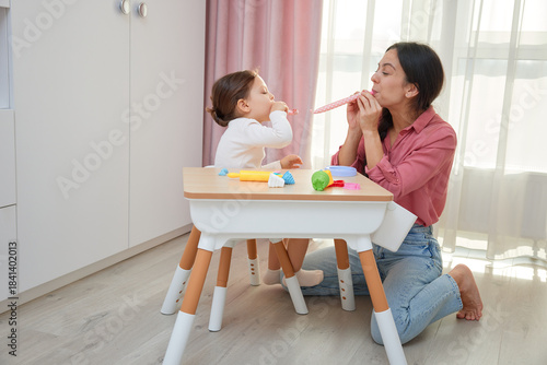Mother and daughter celebrating and playing with party blowers at a small table