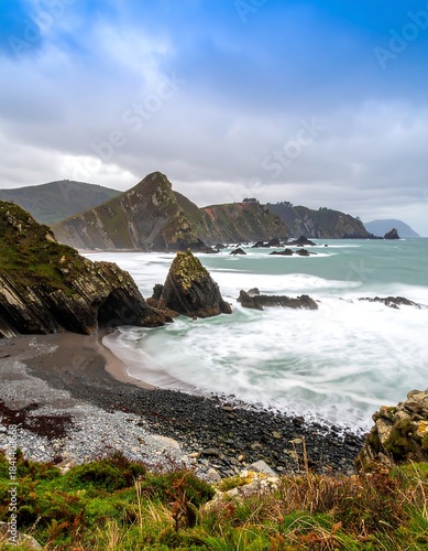 Coastal scene, dramatic waves crashing on a rocky beach, rugged cliffs, overcast sky