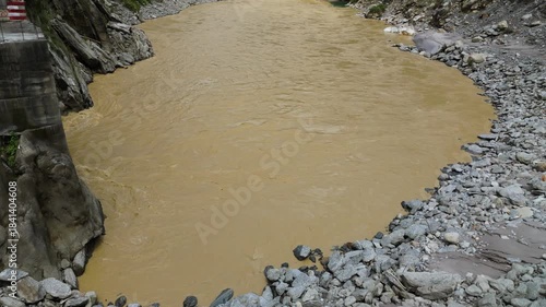 Aerial drone footage of a fast flowing river in Nepal featuring a hydropower water collection infrastructure built into the rocky bank surrounded by dense forest and hills