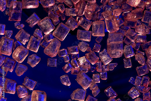 Macro close-up of pink Himalayan salt crystals scattered on a dark background with blue light. Food, seasoning, gourmet, health, and mineral concept.