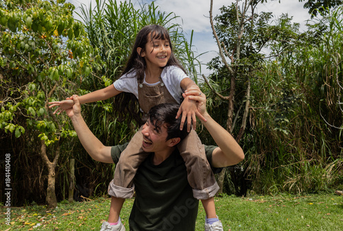 Man carrying his niece on his shoulders as they play happily outdoors in nature, a joyful and tender family moment perfect for scenes of togetherness