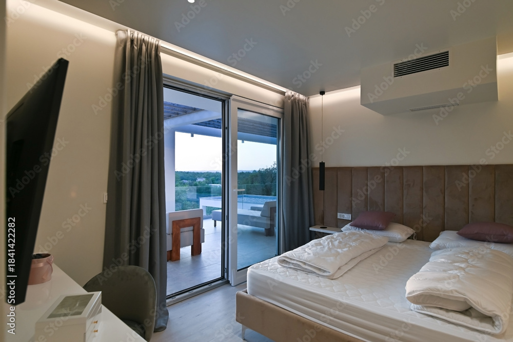 Fototapeta premium Bright, modern bedroom featuring a comfortable bed, sleek desk, and a large sliding glass door opening to a private balcony with stunning green landscape views, perfect for relaxation and serene