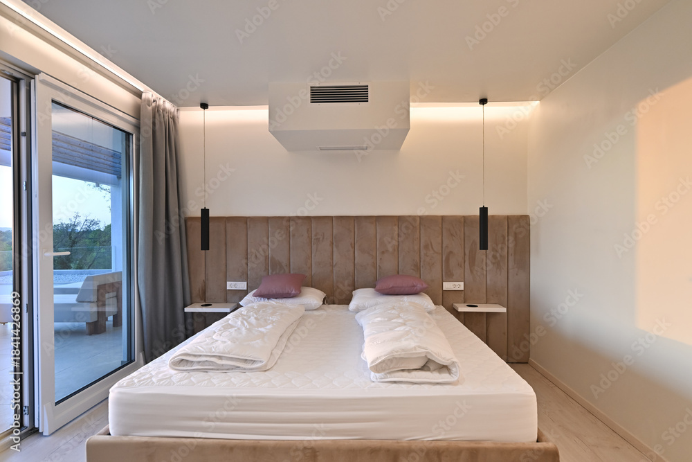 Naklejka premium Bright, modern bedroom featuring a comfortable bed, sleek desk, and a large sliding glass door opening to a private balcony with stunning green landscape views, perfect for relaxation and serene