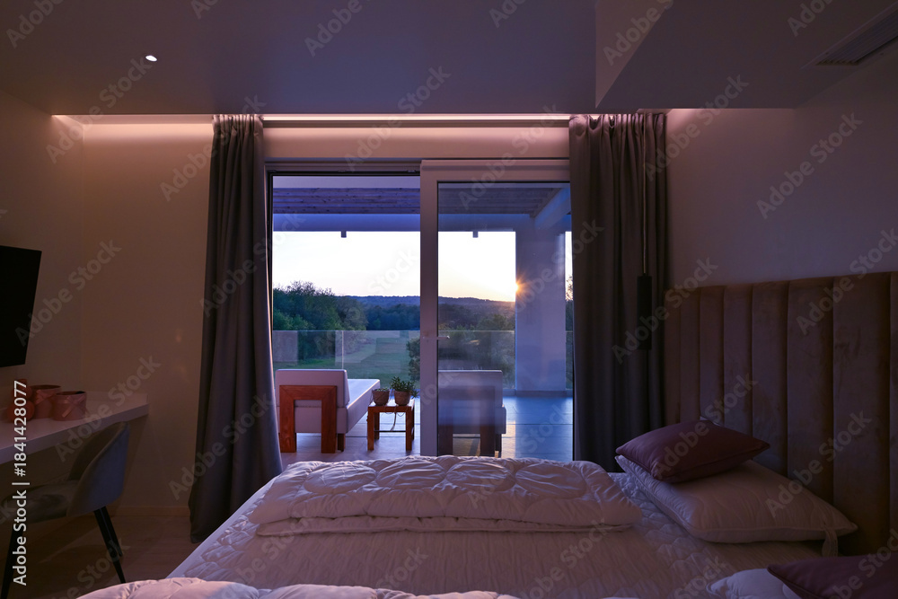 Naklejka premium Bright, modern bedroom featuring a comfortable bed, sleek desk, and a large sliding glass door opening to a private balcony with stunning green landscape views, perfect for relaxation and serene