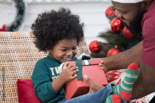 Christmas holiday. Happy family and gift box on Christmas day. African American family opening gift boxes together on Christmas day at home. Father gives gift box to his son