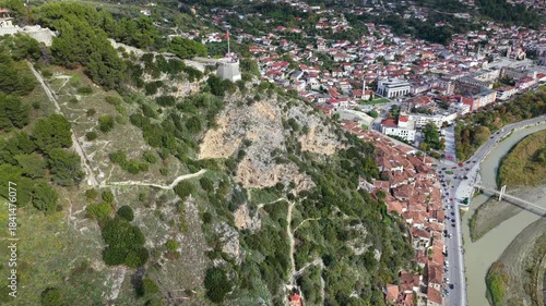 Aerial view of Berat showing hillside homes beneath the rocky slope leading to the castle and the Osum River crossing below.