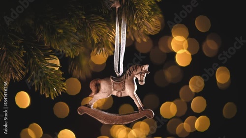 Rocking horse ornament decorating a fir tree branch, creating a heartwarming and nostalgic holiday atmosphere with warm bokeh lights in the background