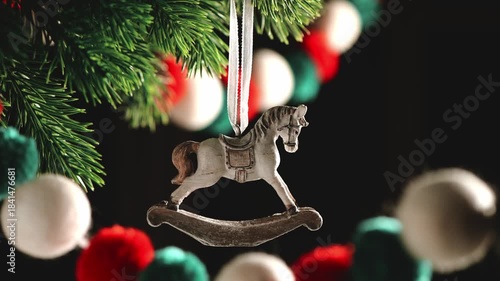 Rocking horse ornament hanging on a green fir tree branch, celebrating the holiday season with colorful background lights creating a festive atmosphere