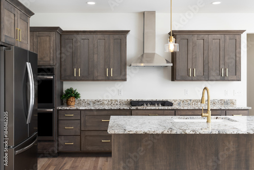 A kitchen detail with a gold faucet on a granite countertop, dark wood cabinets, stainless steel appliances, and gold pendant lights hanging above the island.