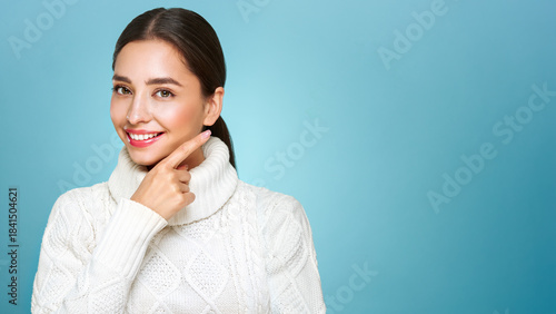 Portrait of young happy beautiful woman, shows with hands to the side copy space, isolated on blue background in a warm white sweater. Concept of winter promo sale