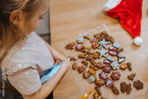 Child decorates gingerbread cookies during festive season in cozy kitchen