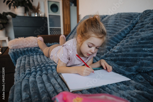 Girl drawing in a notebook while relaxing on a blue couch in a cozy living room