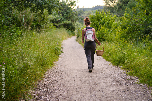Billede på lærred Woman walking on path carrying basket foraging in nature