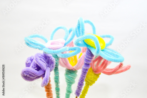 Colorful bouquet of handmade flowers crafted from pipe cleaners (fuzzy wires) in pastel and neon colors, against a white background. Concept for children's craft, DIY, and creativity.